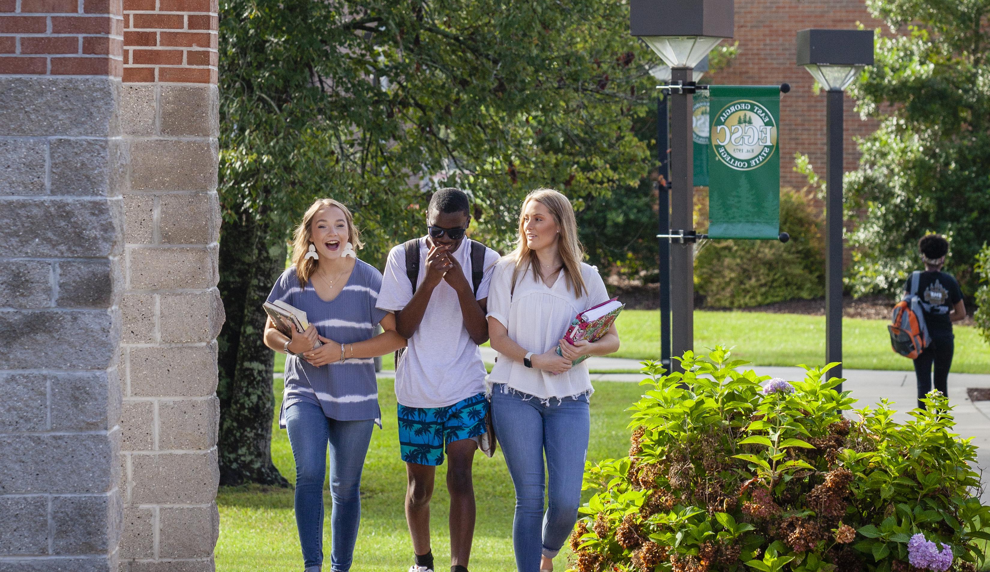 two female students 和 a male student laughing while walking through campus